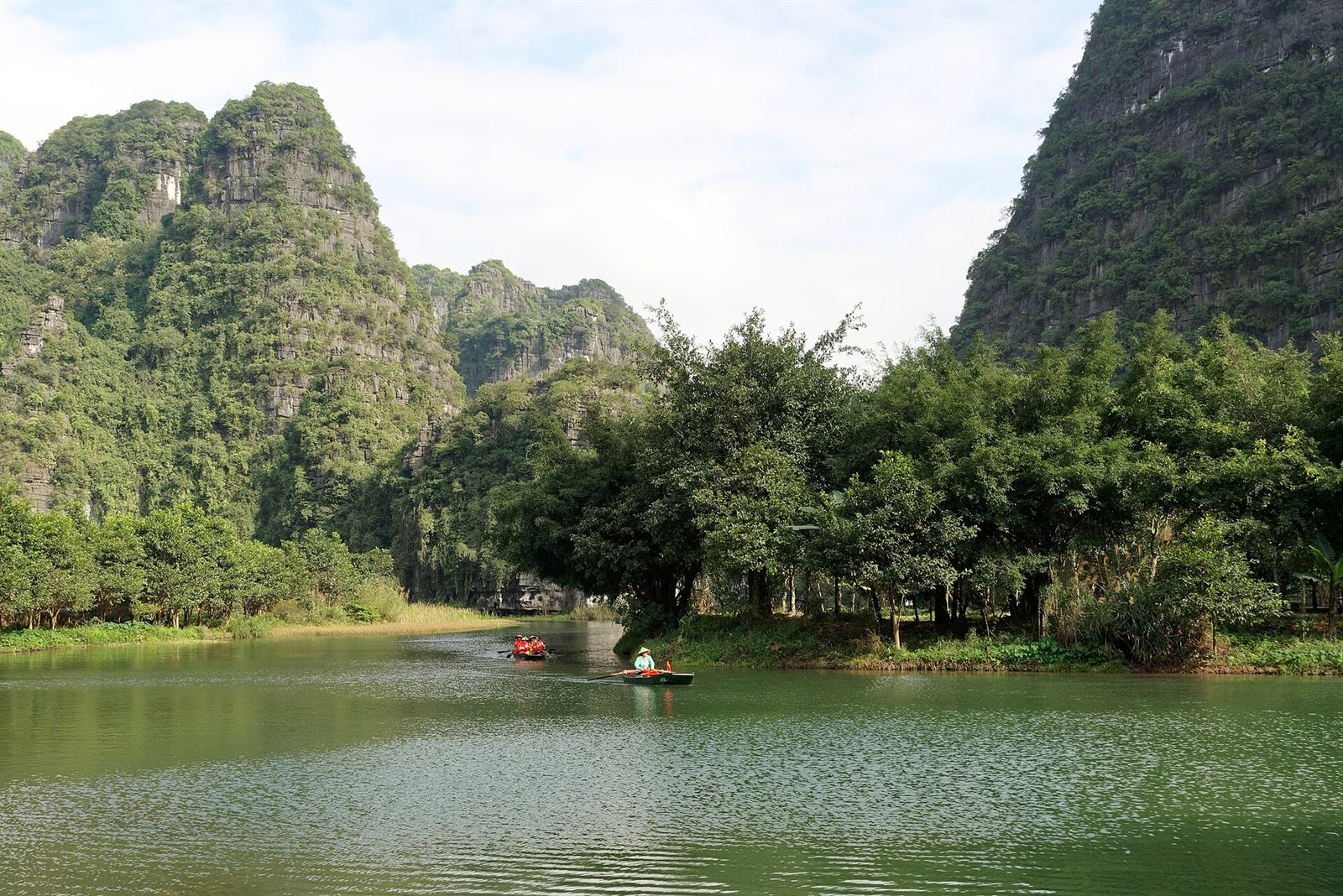 Thuyền nan chở khách trôi trên dòng sông xanh giữa những vách núi đá vôi ở Tràng An, Ninh Bình